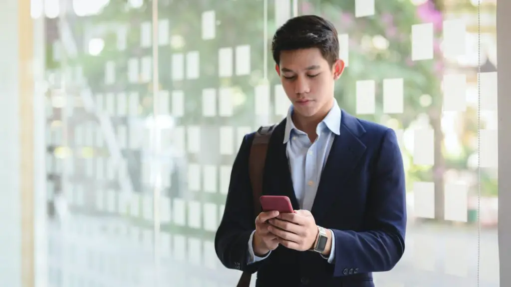 A young male brunette MBA graduate in a business suit without a tie looking into his smartphone