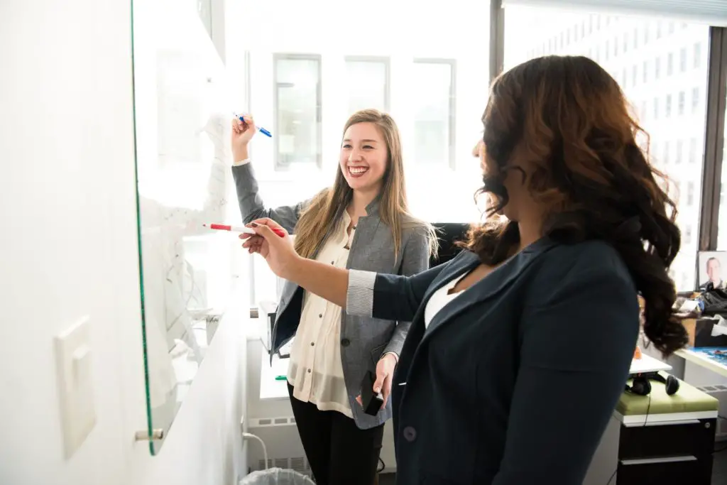 Two MBA female students in business casual outwear candidates drawing on a board during class