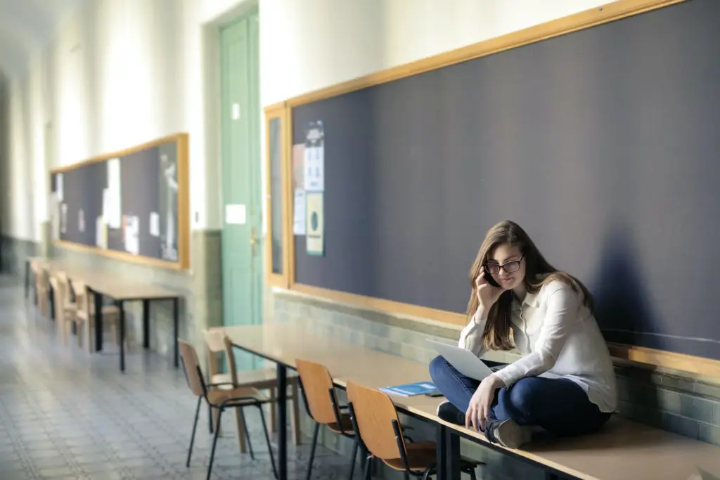 A female law student in jeans and white sweater sitting on desk by the blackboard in law school